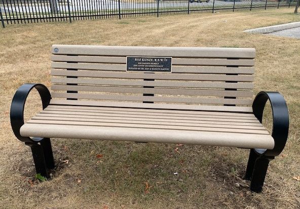 Beige memorial bench with plaque on the back in memory of a loved one that supports the Arbour Fund