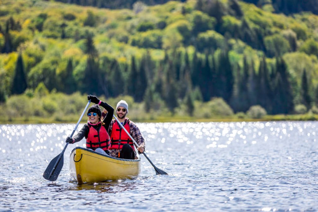 Two people canoeing on a lake with trees in the background